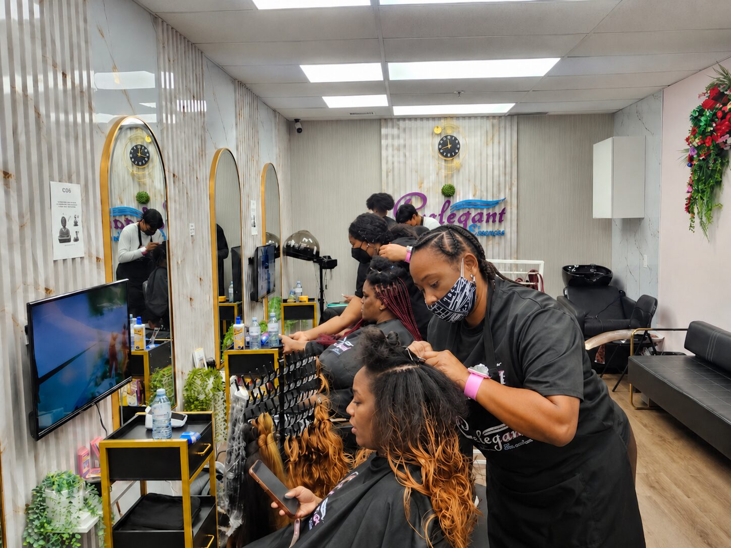 Braiders working on clients at several stations in the Celegant Hair Edmonton salon, wearing branded aprons and face masks